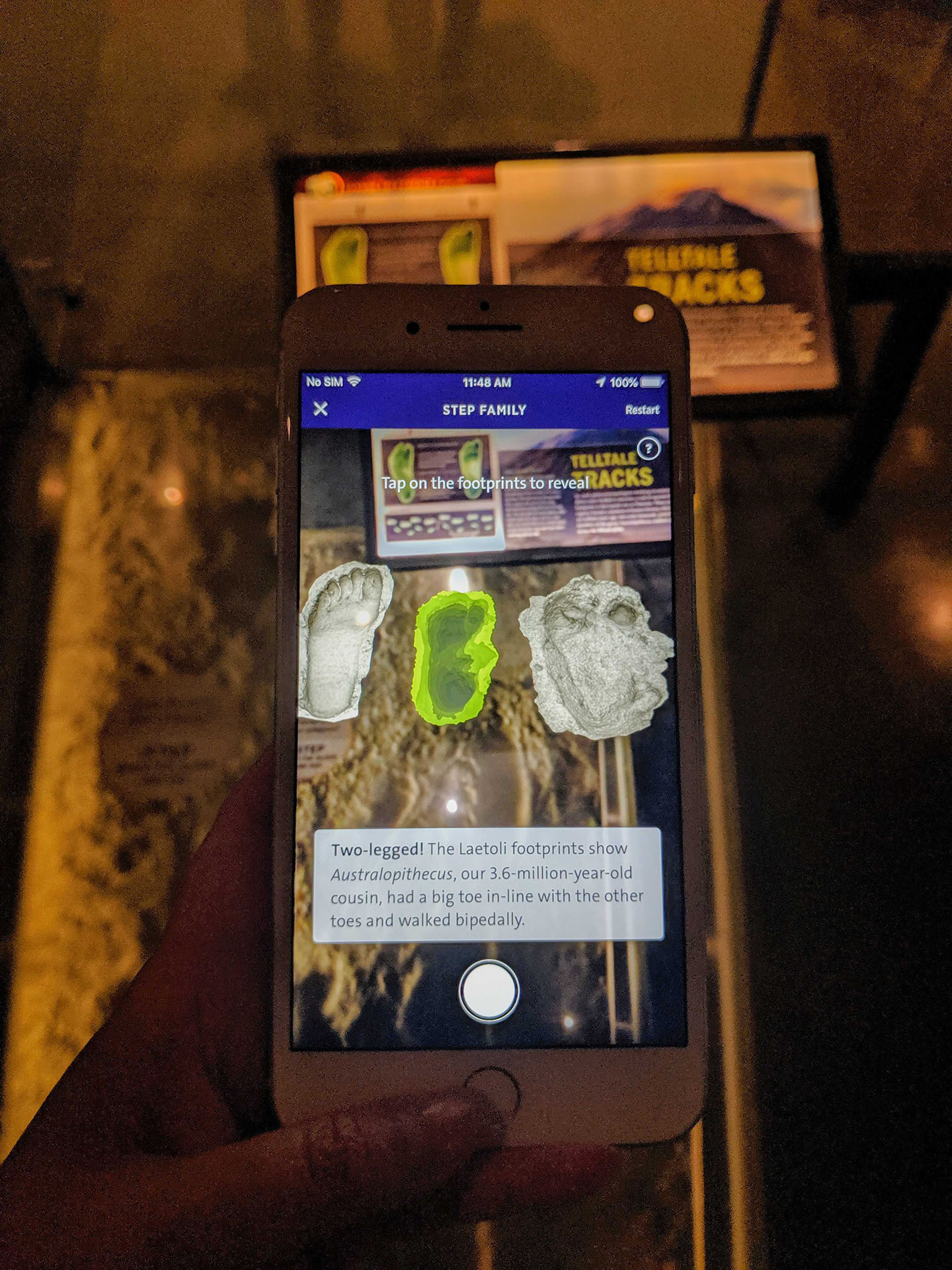A screenshot of a hand holding a smartphone that is displaying three different footprints overlaid in the Museum's physical exhibits